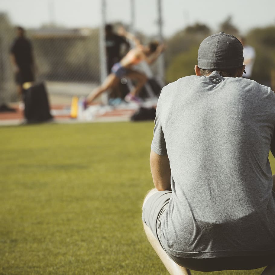 man in gray T-shirt crouching and watching on woman running on field HD wallpaper