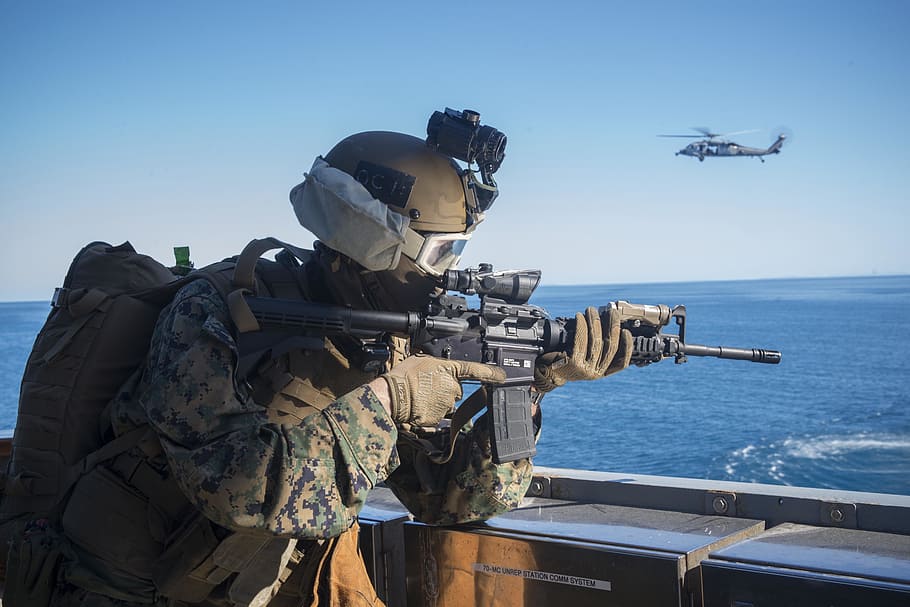 man carrying black M4A1 carbine near gray helicopter, marine expeditionary unit