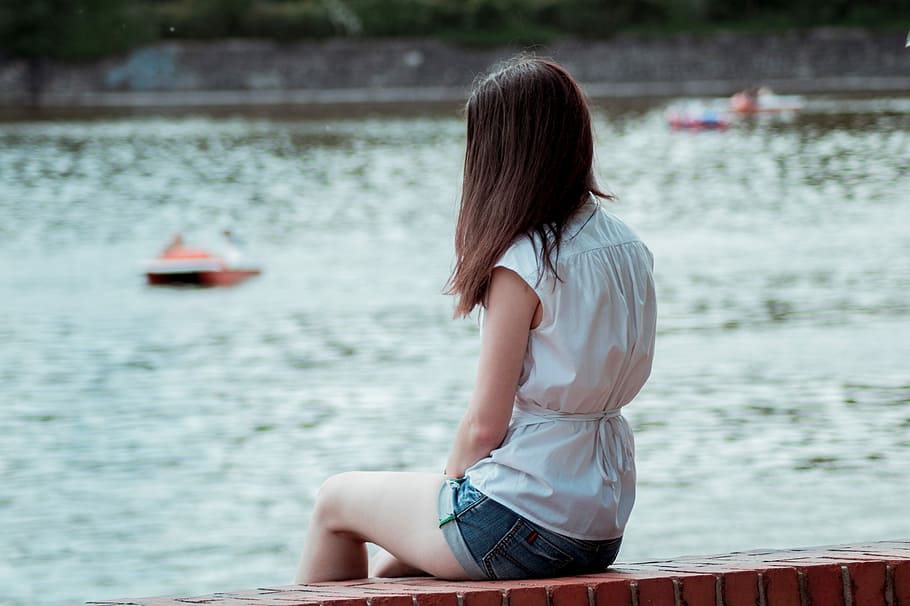woman wearing white sleeveless dress sitting on brown brick near body of water during daytime HD wallpaper