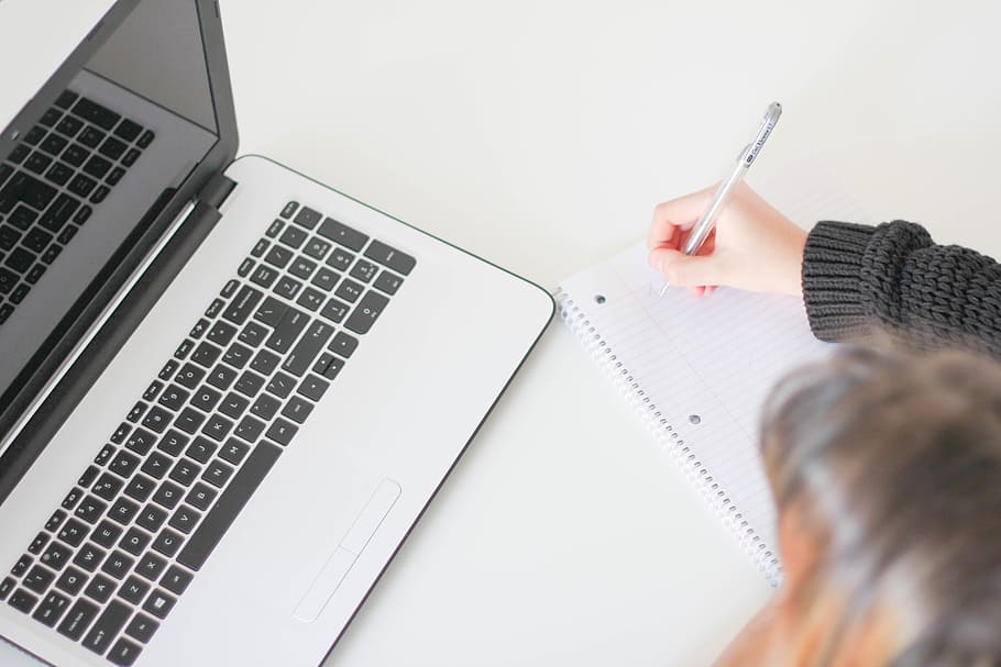 person writing on white lined paper beside laptop, apple, macbook HD wallpaper