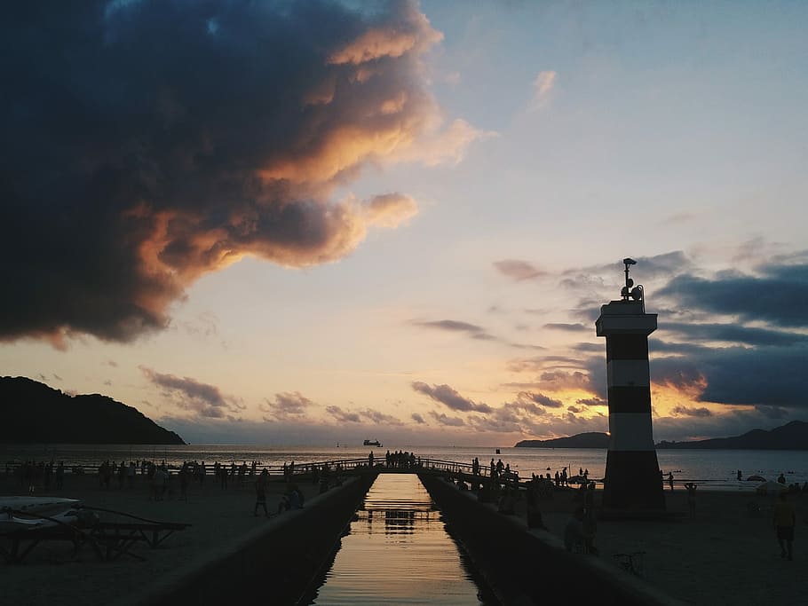 white and black lighthouse under cloudy sky, people standing near body of water HD wallpaper