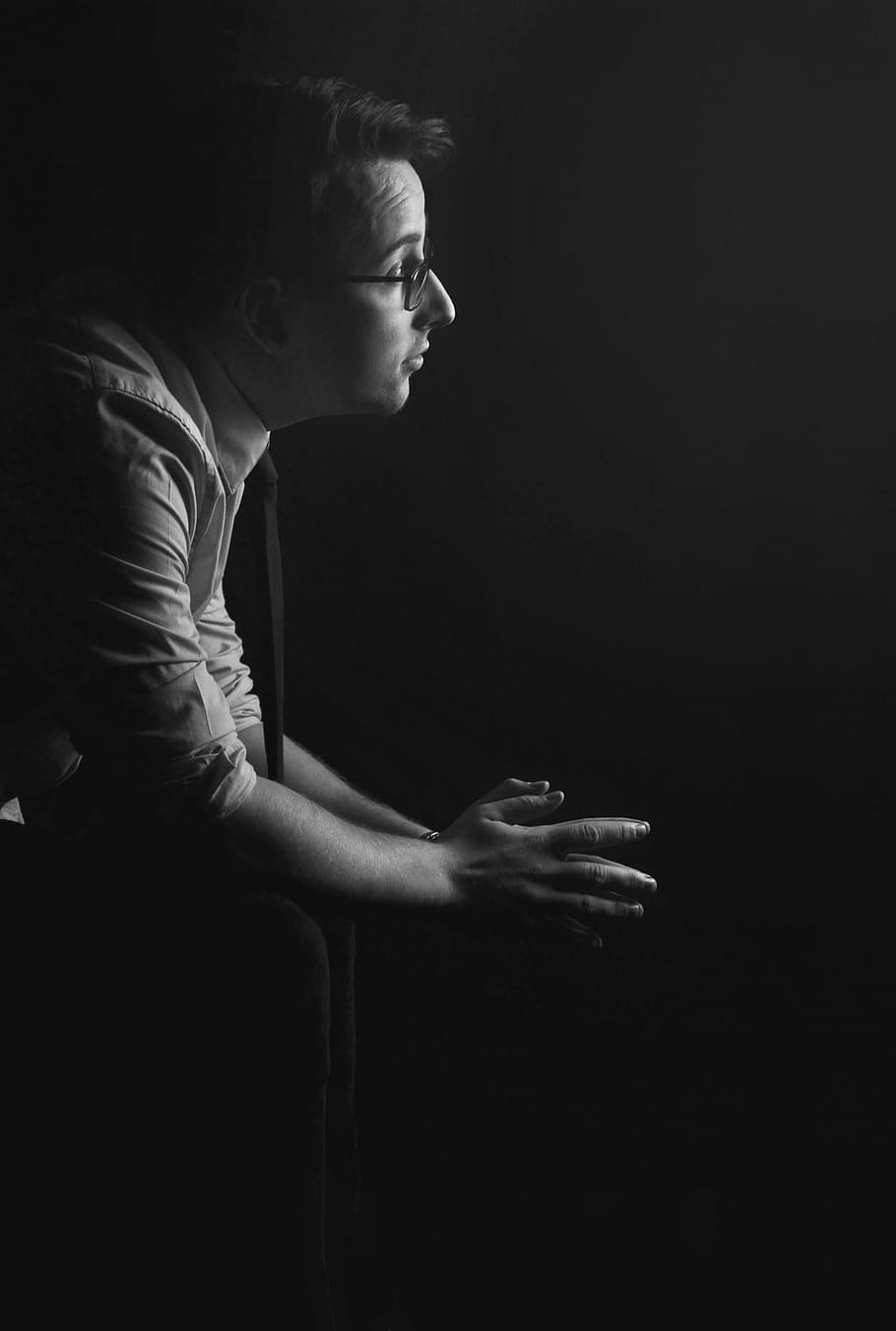 greyscale photography of sitting on chair while wearing eyeglasses