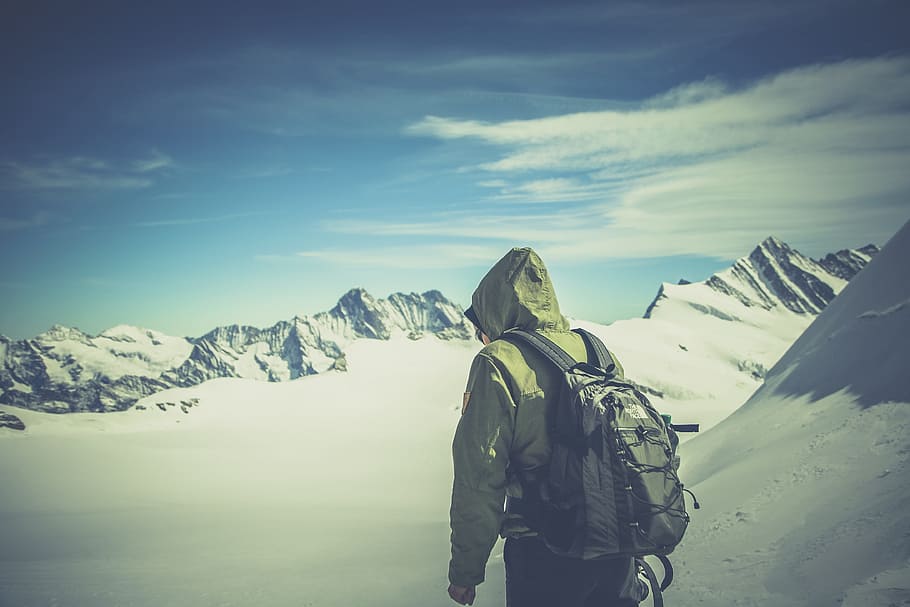 person in brown hoodie carrying black backpack on field cover by snow during daytime HD wallpaper