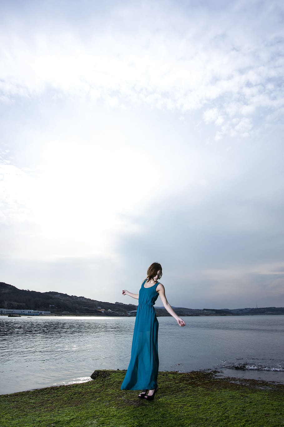woman wearing teal sleeveless long dress standing on grass field near body of water