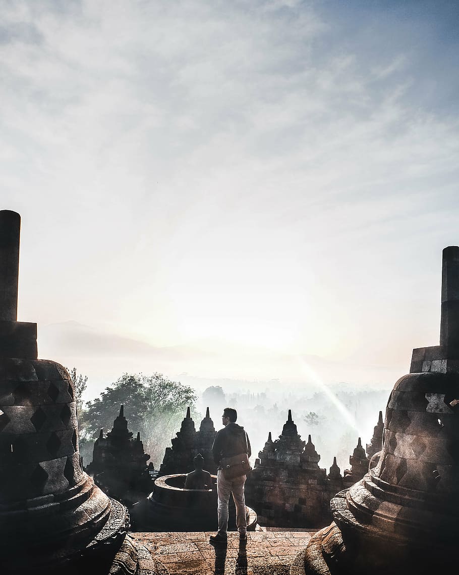 man standing on stair beside statues against light during daytime HD wallpaper