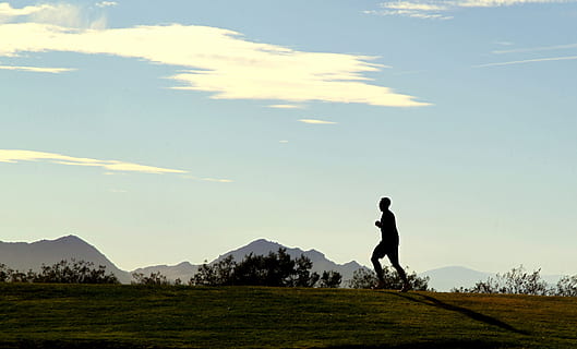 silhouette of man running on top of hill under white clouds at daytime HD wallpaper