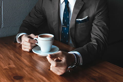 man holding cup filled with coffee on table, man in suit holding mug with coffee sitting on chair front of table in room HD wallpaper