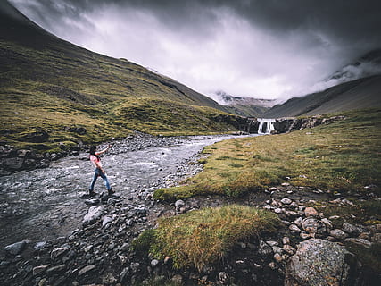 woman in blue jeans crossing river, woman wearing pink shirt and blue denim jeans standing on river between green grass field under gray and white cloudy sky HD wallpaper