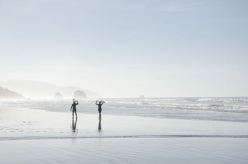 two men carrying surfboards near body of water, two person walking by the seashore during daytime HD wallpaper