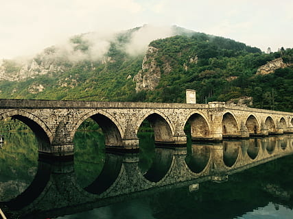 brown concrete bridge during day time, gray concrete bridge over body of water near mountain under white sky at daytime HD wallpaper