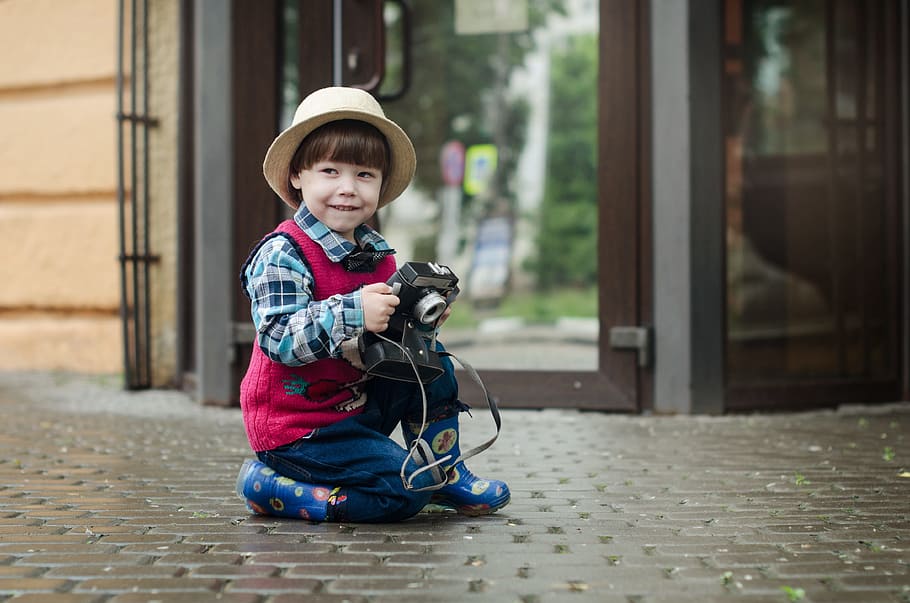 bot sitting on floor holding camera, boy, hat, kids, baby, street HD wallpaper