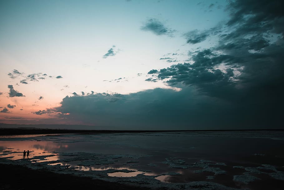 body of water under blue and white cloudy sky, silhouette of man and woman standing on sea shore during sun set HD wallpaper