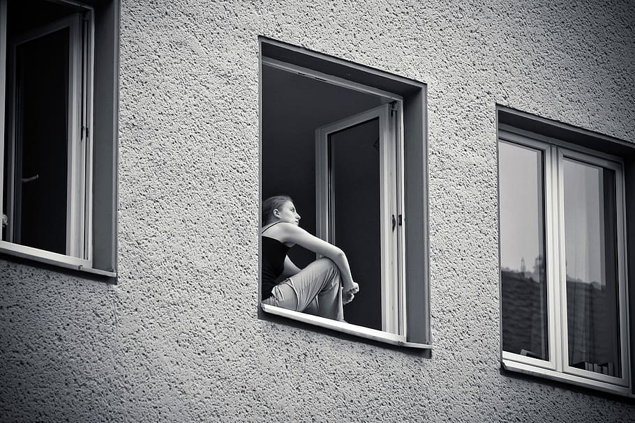 grayscale photo of woman standing beside window, building, home