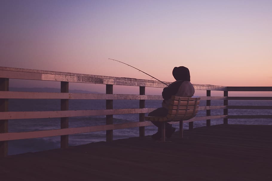 photo of person sitting on bench and holding fishing rod, hooded HD wallpaper
