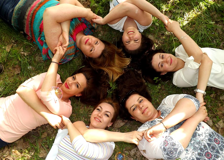 six women forming circle laying on green grass holding their hands each other