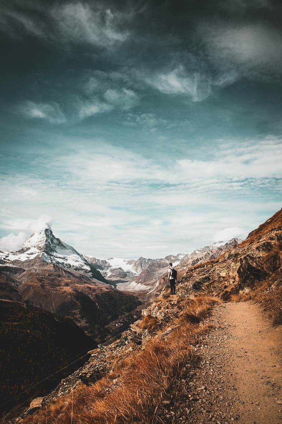 man standing while looking at mountain range, man carrying black backpack standing on cliff of mountain HD wallpaper