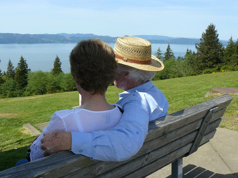 man in blue long-sleeved top beside woman in white top sitting in brown bench