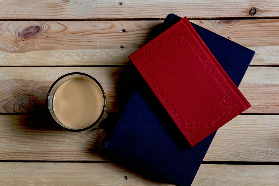 red book on top of blue book beside cup, desk, table, notebooks