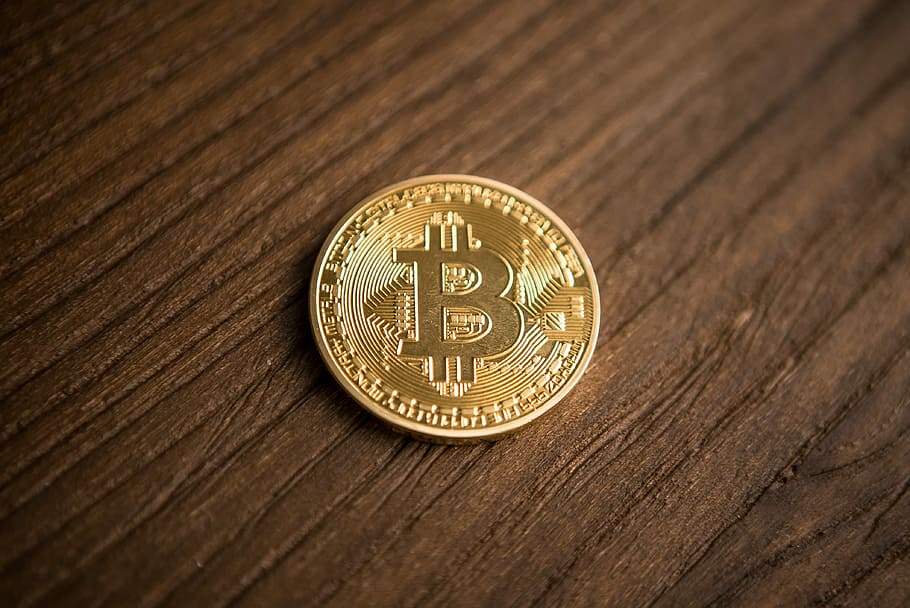 Bitcoin cryptocurrency coin, round gold-colored Bitcoin coin on brown surface