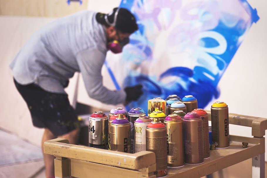 paint sprays on table in front man painting on wall, paint spray bottles on table HD wallpaper