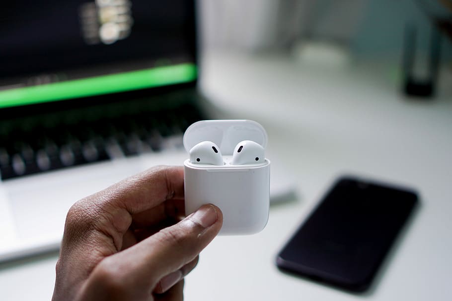 person holding wireless earbuds with charging case, person holding white Apple AirPods with charging case