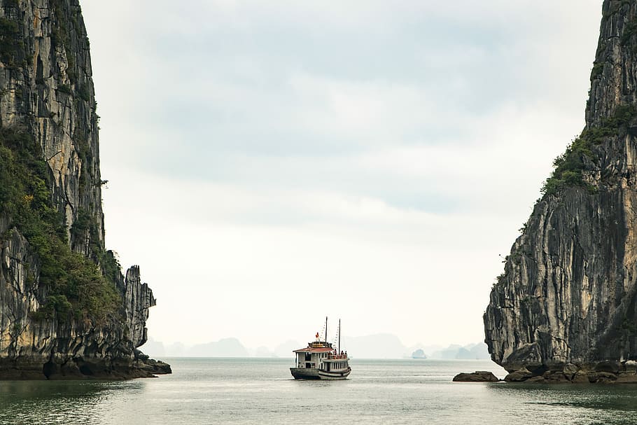 white watercraft on body of water, brown and red boat sailing in the middle of two rock cliffs HD wallpaper