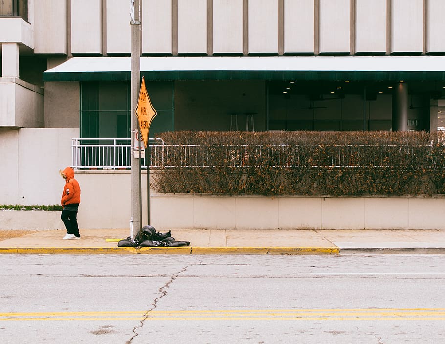 person standing on sidewalk, man wearing orange hooded jacket on sidewalk during daytime HD wallpaper