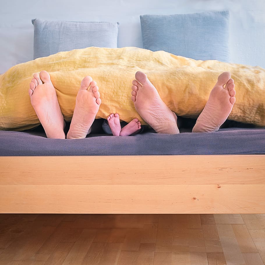 three people underneath yellow bed blanket, three feet hiding on brown blanket