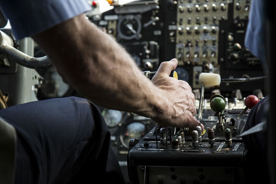 person operating black audio mixer, person sitting on cockpit holding black and white lever HD wallpaper