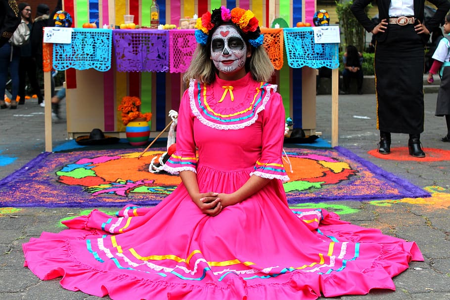woman wearing pink dress kneeling on floor with face paint, offering