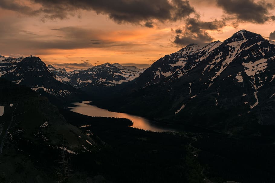 body of water surrounded by black and white mountains under gray sky at golden hour, black and white mountain with body of water during golden hour HD wallpaper