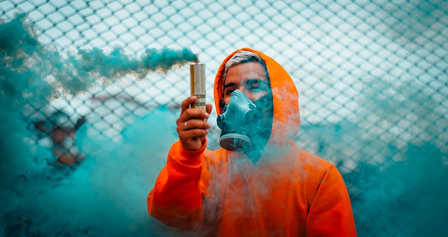 man holding blue smoke flare during daytime, men's orange hoodie