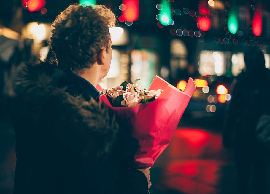 man in black faux fur coat holding bouquet of floweers, person holding flower bouquet at night