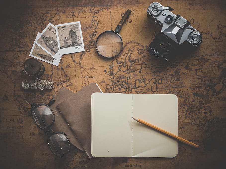 black MILC camera beside magnifying glass on brown map printed surface