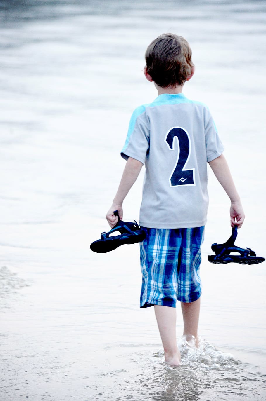 photo of boy holding sandals and walking on body of water during daytime HD wallpaper