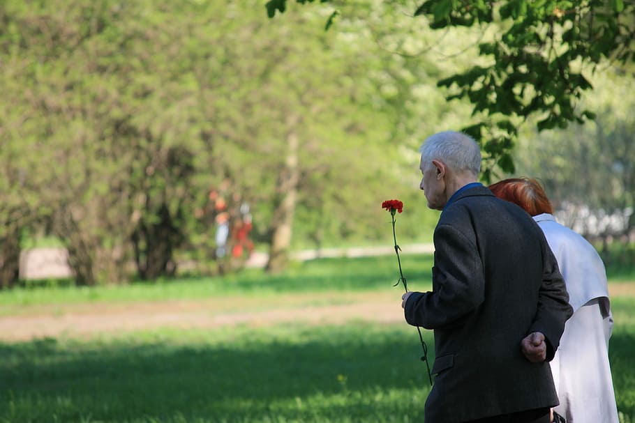 man holding red petaled flower beside woman while walking during daytime HD wallpaper