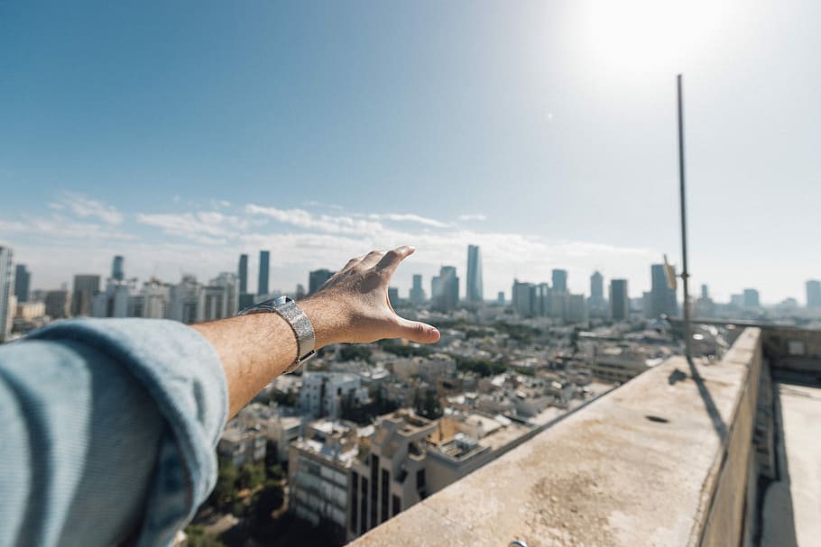 photo of person's hand, person in denim long-sleeved top while near cliff building HD wallpaper