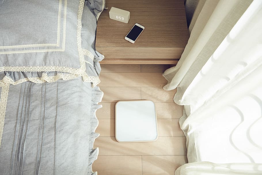 smartphone on brown side table beside bed, square white panel on brown wooden surface HD wallpaper