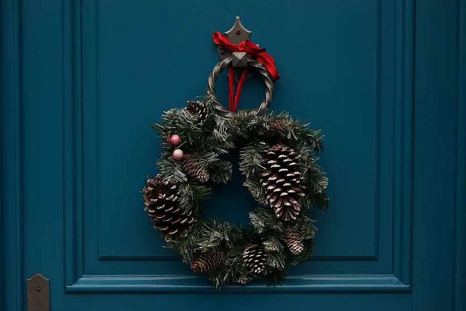 green and brown christmas wreath, green and brown pine cone wreath hanging on black metal door knocker of blue wooden door