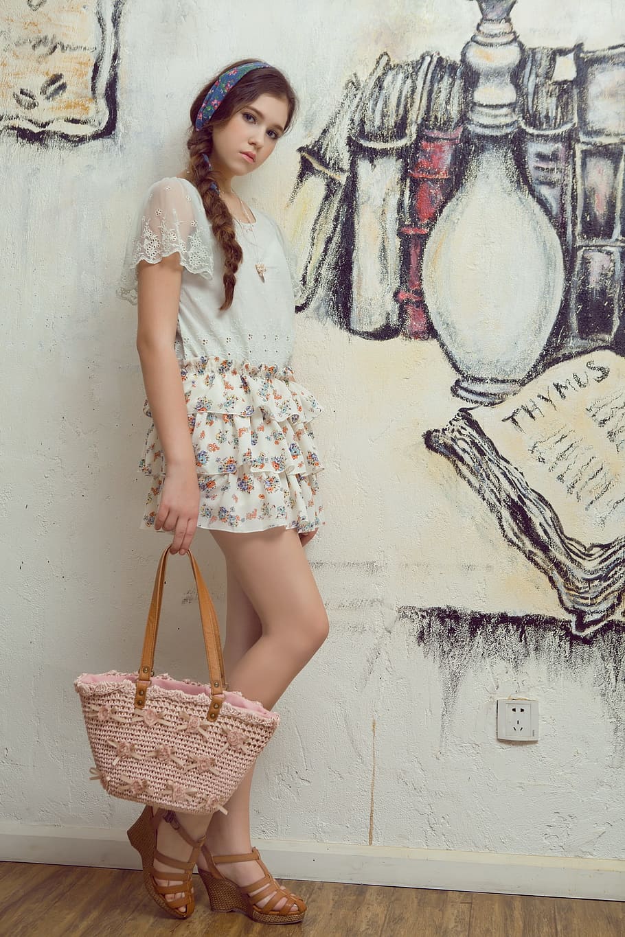 woman holding pink and brown tote bag while leaning on white painted wall