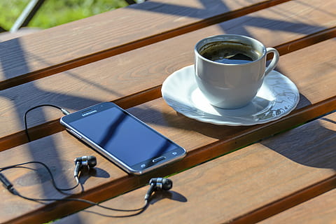 black Samsung Android smartphone with turned-off screen beside cup of coffee on top of brown wooden surface HD wallpaper