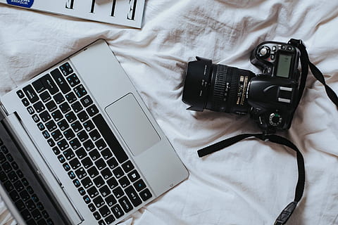 Silver laptop, a camera, magazines and other items on white bed sheets HD wallpaper