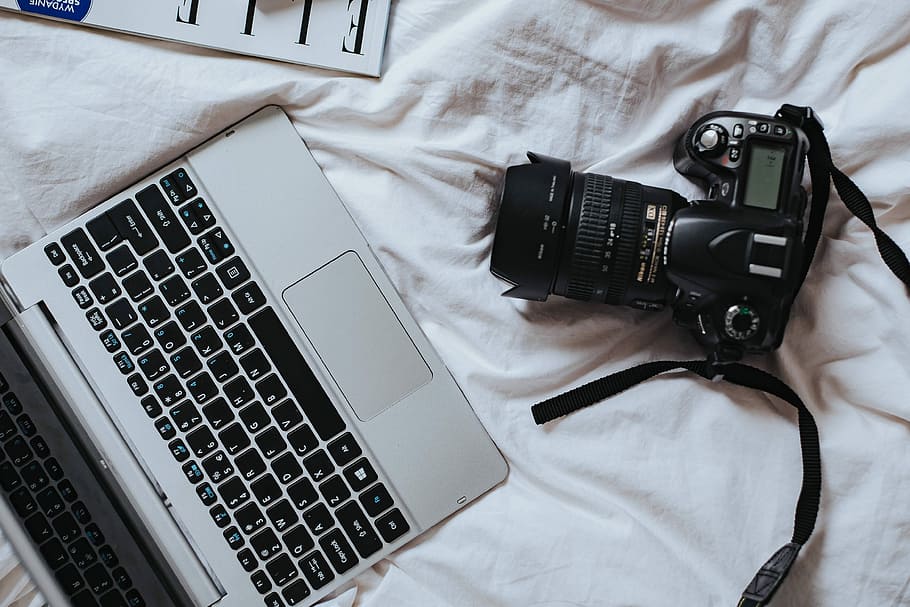 Silver laptop, a camera, magazines and other items on white bed sheets HD wallpaper