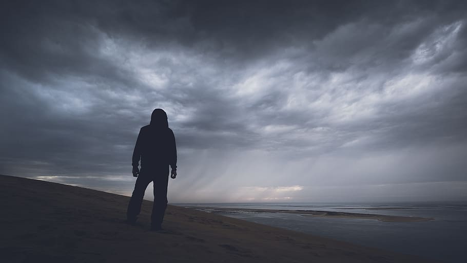 silhouette photography of person under gray clouds, silhouette photography of person standing on sand facing sea HD wallpaper