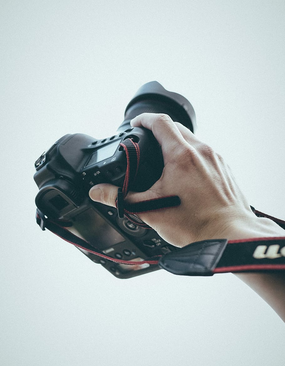person holding camera with camera lens and camera lens hood, person holding black Canon DSLR camera HD wallpaper