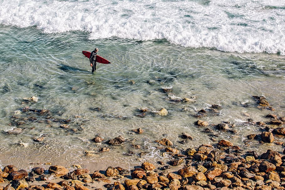 people holding red surfboard standing on body of water, toy plane stuck in brown beach shore HD wallpaper