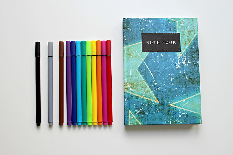 assorted-colored pens with blue and teal Note Book, colour pencils