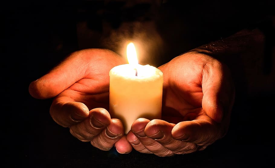 person holding pillar of candle with two hands, open, candlelight