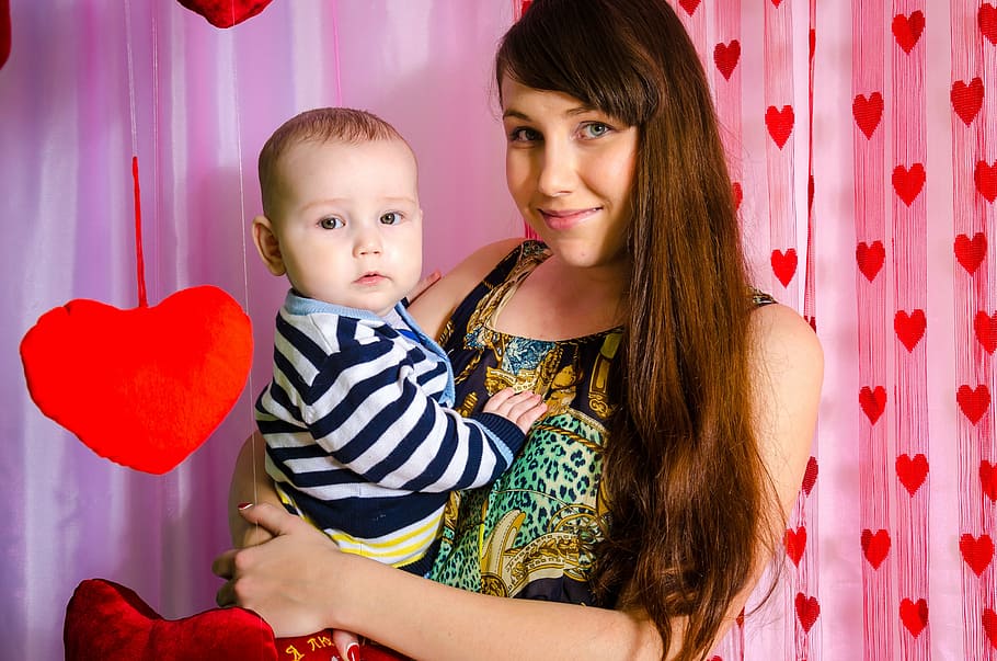 smiling woman carrying her child inside room with heart-print curtain