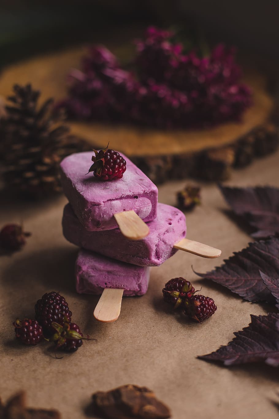 selective focus photography of thee purple ice pops near pine cones, three raspberry popsicles